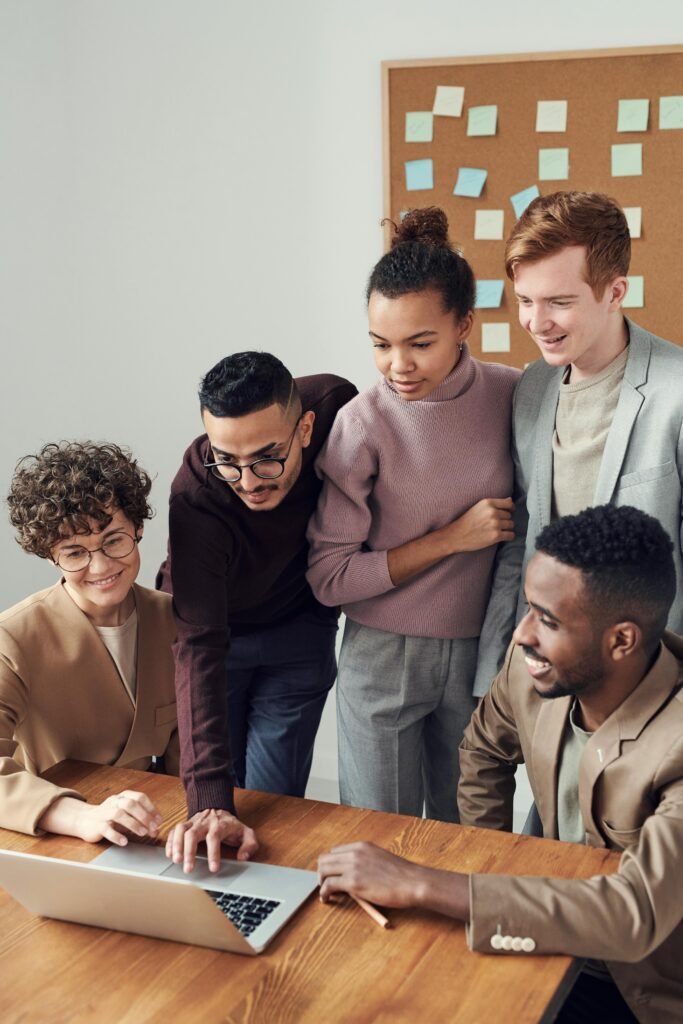 A diverse group of young professionals collaborating around a laptop in a modern office setting.